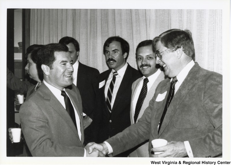 On the left, Representative Nick J. Rahall (D-W.Va.) shakes hands with an unidentified man at an event with a group of unidentified men.