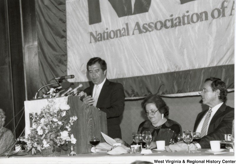 Representative Nick J. Rahall (D-W.Va.) gives a speech at a banquet. The banner behind him reads "National Association of A-".