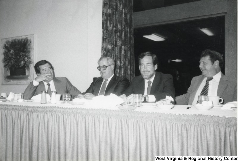 On the far left, Representative Nick J. Rahall (D-W.Va.) sits at a banquet table and talks with three unidentified men.