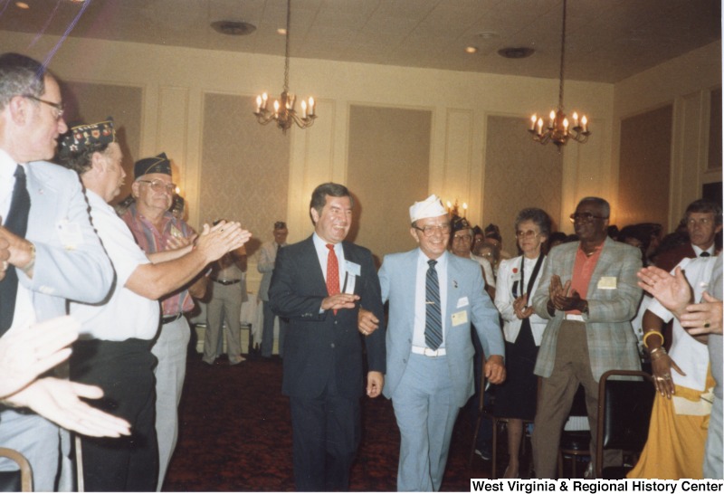 On the right, the American Legion Sergeant at Arms escorts Representative Nick J. Rahall (D-W.Va.) through a crowd of veterans. They are headed the joint session of the American Legion and American Legion Auxiliary Department Convention.