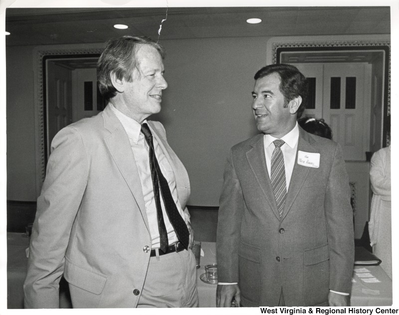 On the right, Representative Nick J. Rahall (D-W.Va.) talks with an unidentified man at an event.