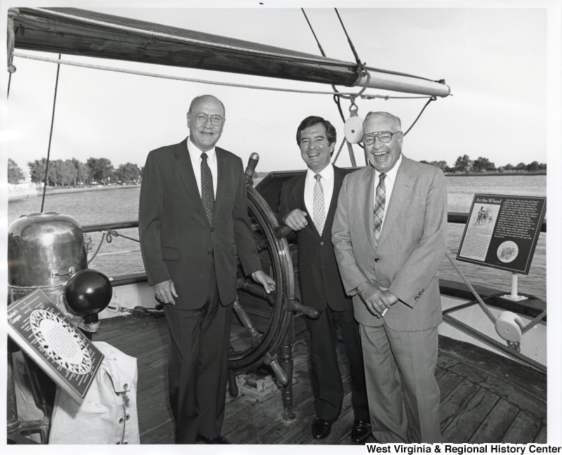 Representative Nick J. Rahall (D-W.Va.) stands between two unidentified men on a boat.