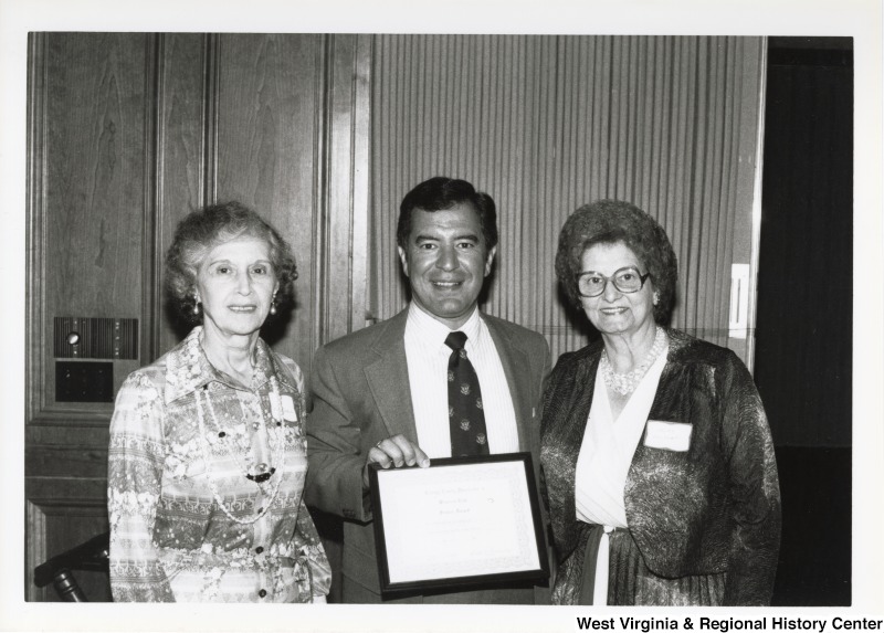 Representative Nick J. Rahall (D-W.Va) smiles for a photograph holding an award between two unidentified women of the Raleigh County Democratic Women's Club.