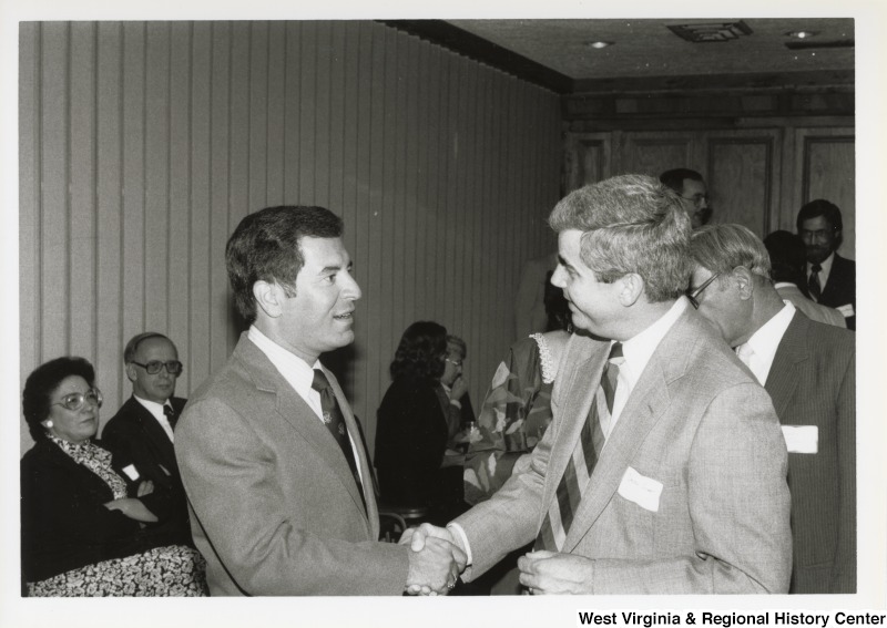 On the left, Representative Nick J. Rahall (D-W.Va.) shakes hands with an unidentified man at an event.