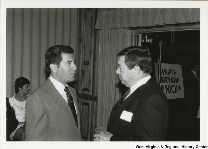 On the left, Representative Nick J. Rahall (D-W.Va.) talks with an unidentified man at his birthday party. A sign behind the two men reads "Happy Birthday Nick."