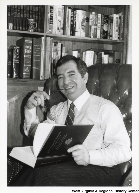 Representative Nick J. Rahall (D-W.Va.) in an office holding a book about John Fitzgerald Kennedy.