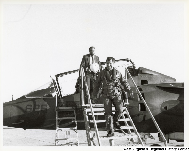 Representative Nick J. Rahall (D-W.Va.), dressed in a fighter pilot's uniform, descends from a plane followed by an unidentified man in a suit.