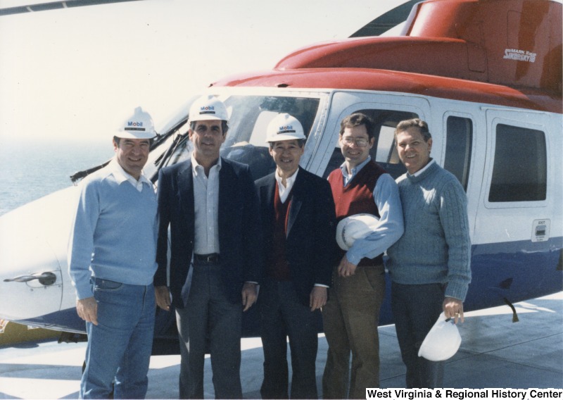 L-R: Representative Nick J. Rahall (D-W.Va.), Representative Tony Coelho (D-Calif.), Representative Bob Matsui (D-Calif.), Representative Alan Mollohan (D-W.Va.), Representative Ronnie Flippo (D-Ala.).The Congressmen wear or hold Mobil Oil hardhats in front of a helicopter while visiting an oil rig in the Gulf of Mexico.