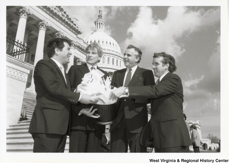 On the far left, Representative Nick J. Rahall (D-W.Va.) holds a bucket filled with papers with three unidentified men in front of the United States Capitol building.