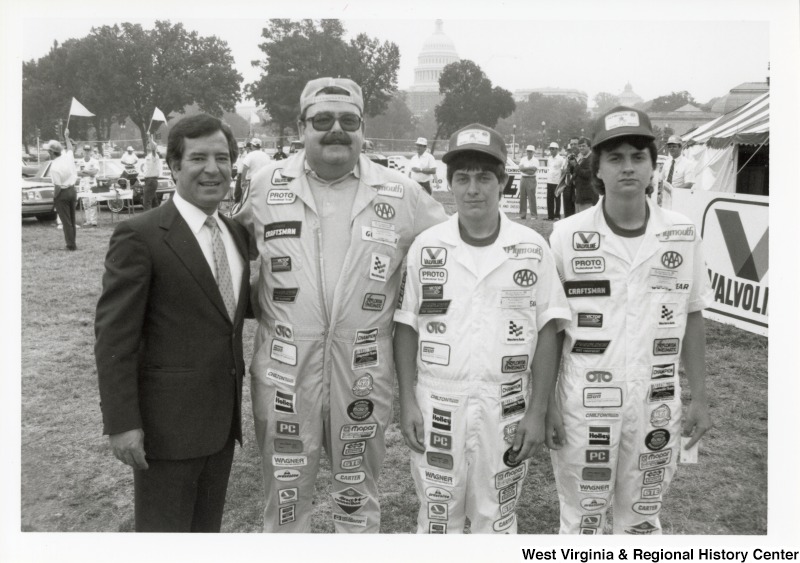 On the far left, Representative Nick J. Rahall (D-W.Va.) stands for a photo with three unidentified car drivers at the Plymouth Trouble Shooting Contest.