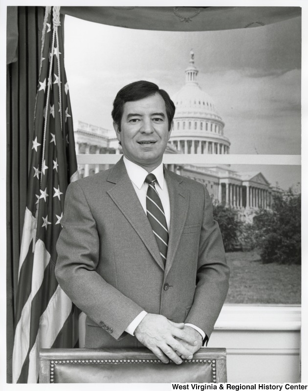 Representative Nick J. Rahall (D-W.Va.) stands behind a desk with the Capitol building in the background.