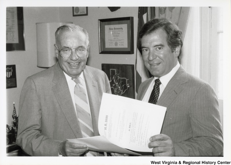 On the right, Representative Nick J. Rahall (D-W.Va.) stands beside an unidentified man in his office holding a House of Representatives legislative bill.