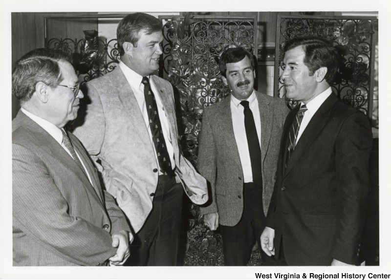 Congressman Nick Rahall speaking with three unidentified people in suits during an official visit to Marshall University.
