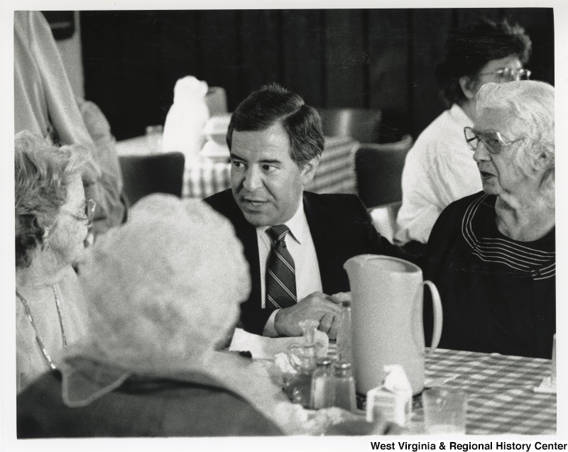 Congressman Nick Rahall (D-WV) speaking with three unidentified senior women at a dinner table.