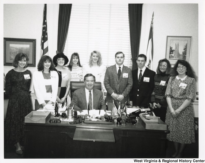 Representative Nick J. Rahall (D-W.Va.) sits behind his desk with a group of nine unidentified people from the Close-Up Washington D.C. program around him.