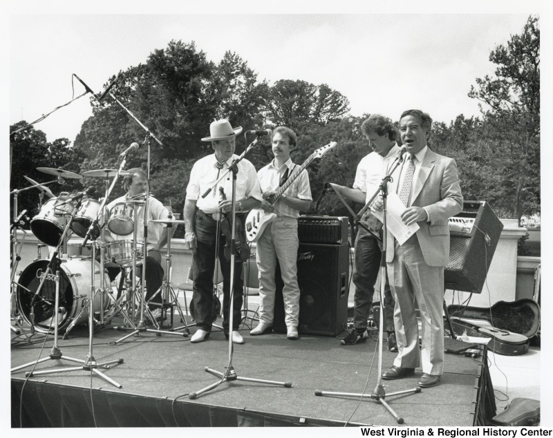 On the right, Representative Nick J. Rahall (D-W.Va.) stands on stage with Everett Lilly & the Clear Creek Crossin' musicians.