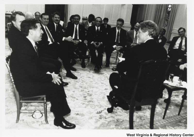 On the left, Representative Nick J. Rahall (D-W.Va.) sits in a group setting and talks with President Bill Clinton.