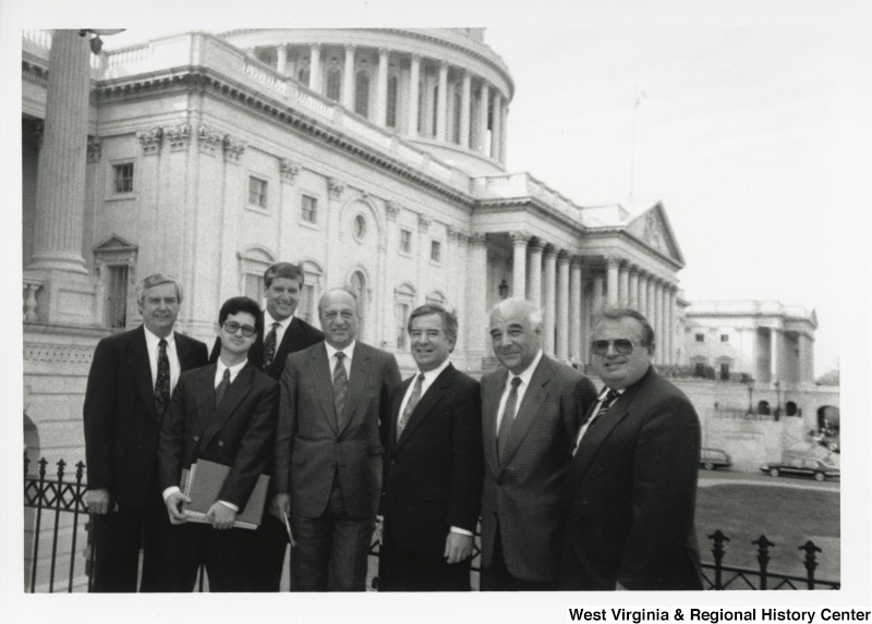 Third from the right, Representative Nick J. Rahall (D-W.Va.) stands for a photograph with six unidentified men in front of the United States Capitol building.