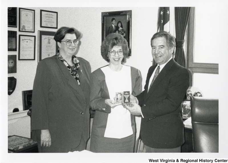 Congressman Nick Rahall (D-WV) holding a plaque with two unidentified women in his office.