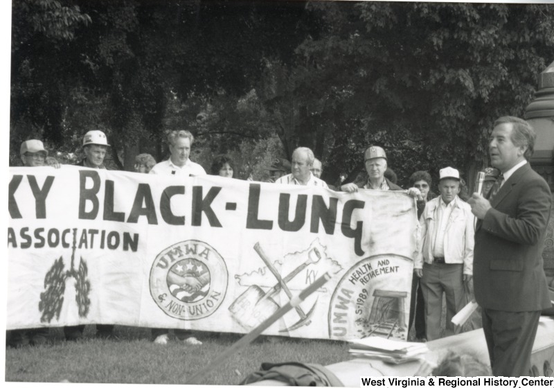 Congressman Nick Rahall (D-WV) speaking at a Black Lung Association rally at the United States Capitol Complex. A group of unidentified Black Lung Association members are in the background holding a banner.