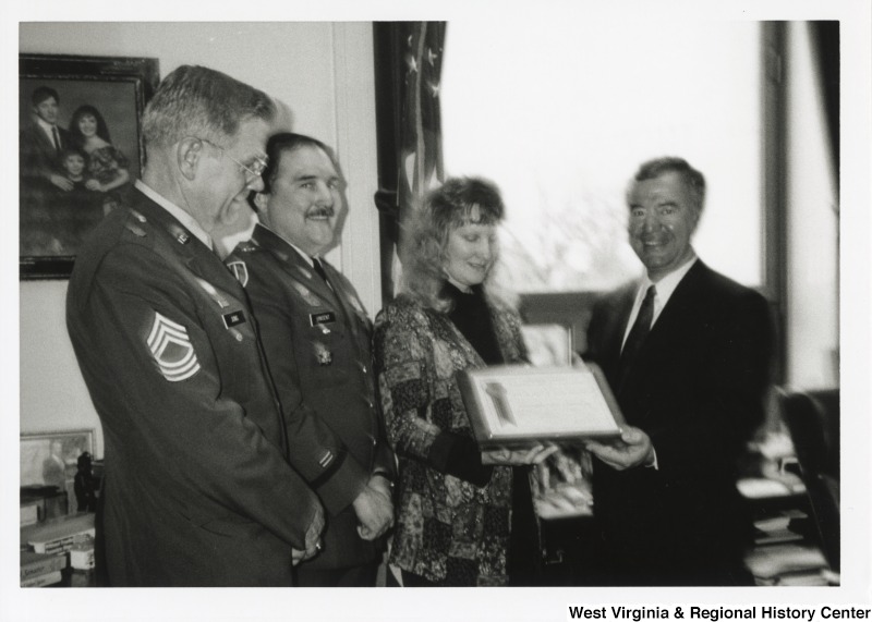L-R: Master Sergeant Jung, Colonel Vincent, Carla Leslie, Representative Nick J. Rahall (D-W.Va.)The four stand in Congressman Rahall's office while the men present Leslie with a flag.