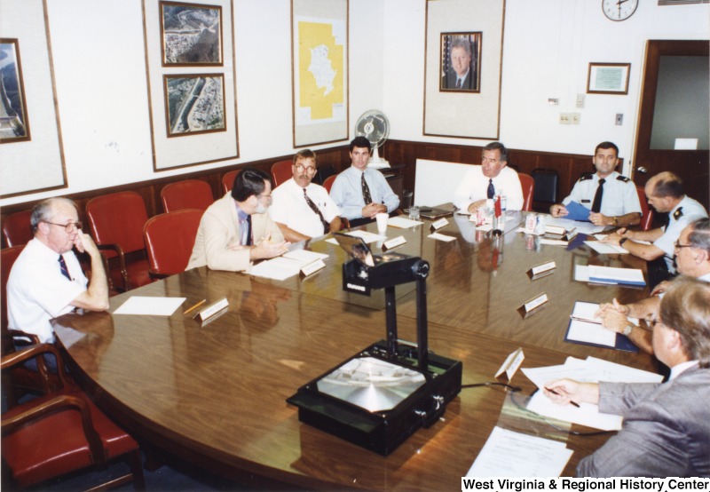 Representative Nick J. Rahall (D-W.Va.) sits at the end of a table surrounded by unidentified men of the Army Corps of Engineers.