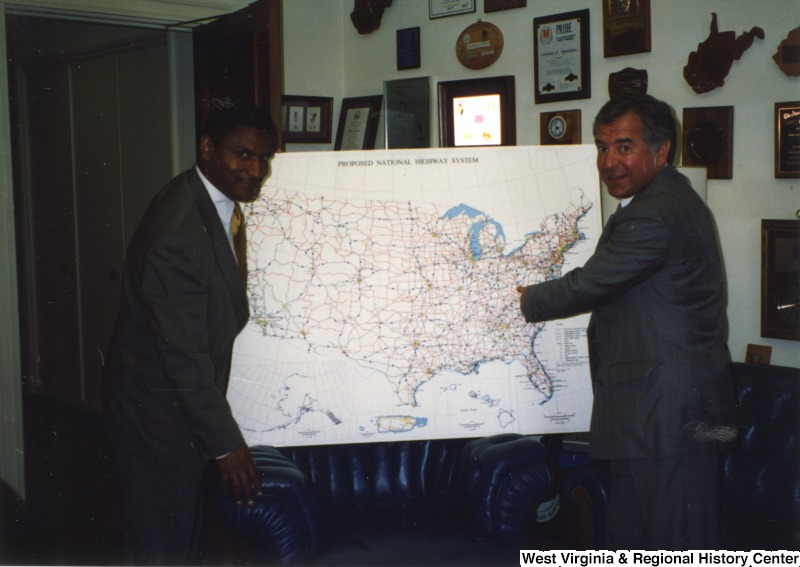 On the right, Representative Nick J. Rahall (D-W.Va.) stands beside a map that reads "Proposed National Highway System" with an unidentified man on the other side.