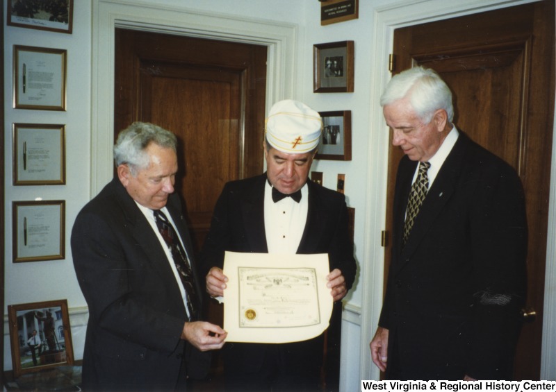 Representative Nick J. Rahall (D-W.Va.) stands between two unidentified men wearing a masonic hat and holding a certificate.