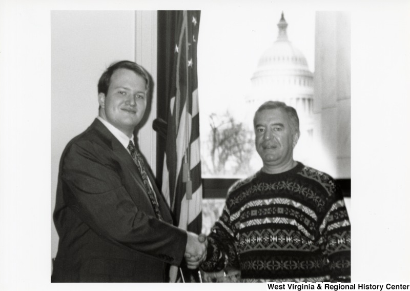 On the right, Representative Nick J. Rahall (D-W.Va.) shakes hands with an unidentified young man.