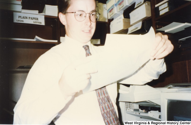 An unidentified man in an office stands holding papers.
