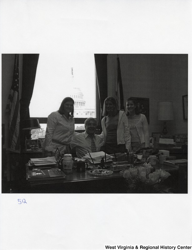 Second from the left, Representative Nick J. Rahall (D-W.Va.) sits at his disk for a photograph with three unidentified women.