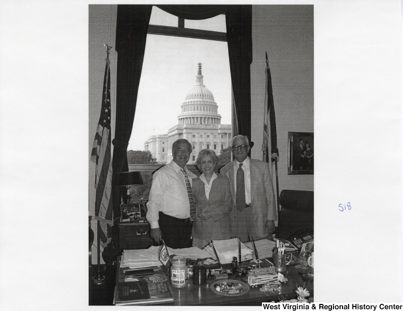 On the left, Representative Nick J. Rahall (D-W.Va.) stands in his office for a photograph with an unidentified man and an unidentified woman.