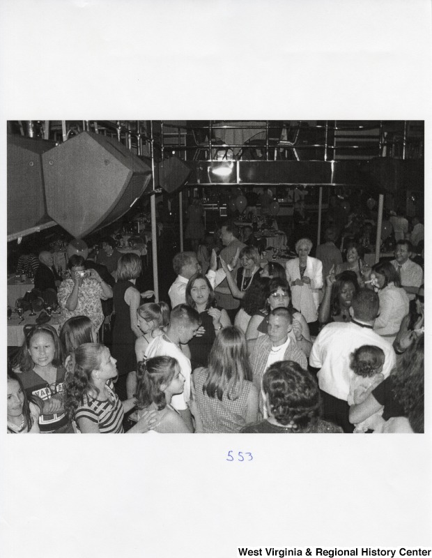 A large crowd of unidentified people dance together on a dance floor at a party.