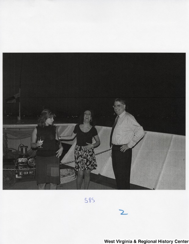 Two unidentified women and an unidentified man laugh on the bow of a boat at a party.