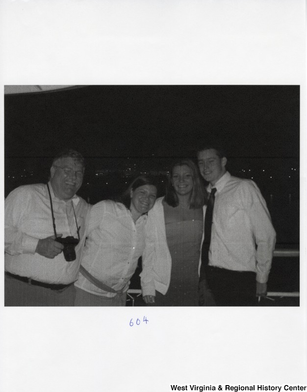 Two unidentified men and two unidentified women stand for a photograph at a party while one holds a camera.