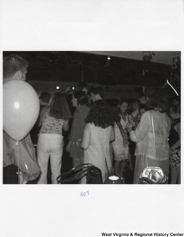 A large group of unidentified people dance together on a dance floor at a party with balloons.
