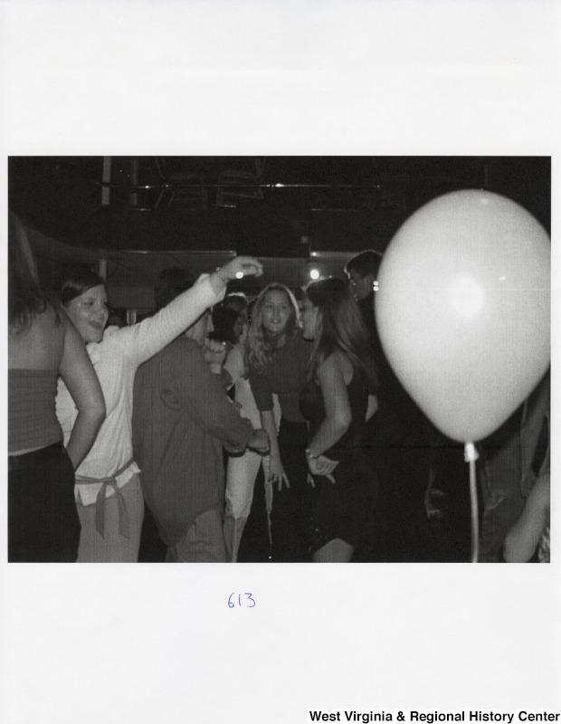 A large group of unidentified people dance together at a party with balloons.