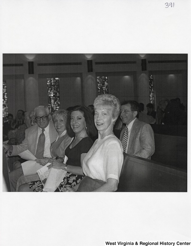 Four unidentified people sit in a pew and smile for a photograph at an event.
