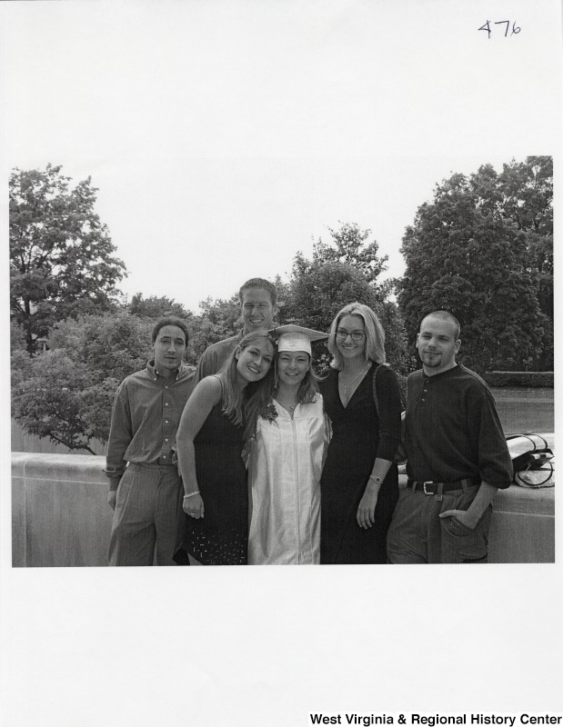 Suzanne Rahall, wearing her graduation regalia, stands in the middle of a group of five unidentified young people.