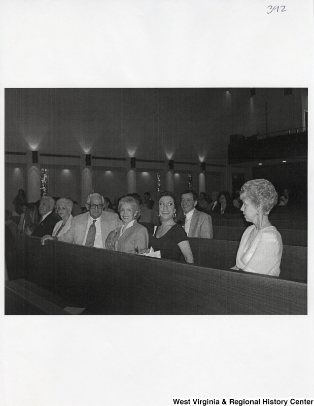 A group of seven unidentified people sit in pews at an event.