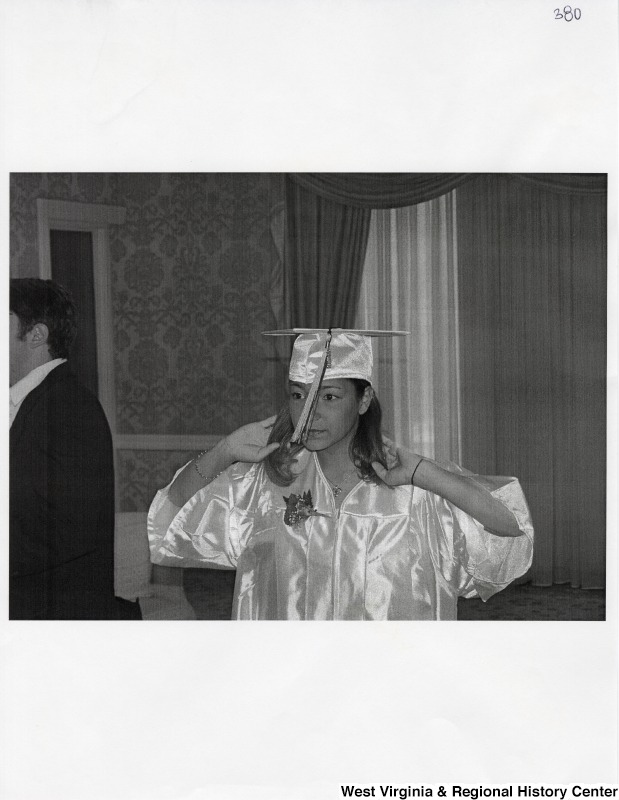 Suzanne Rahall stands in her graduation regalia and fixes her hair.