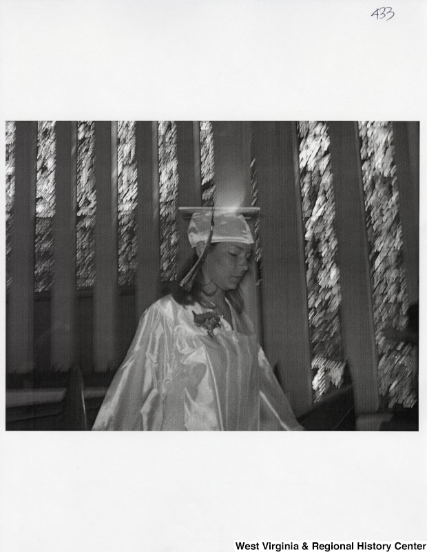 Suzanne Rahall walks in front of the camera in graduation regalia at her commencement ceremony.