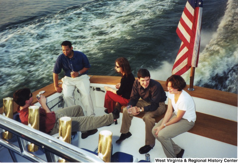 Three unidentified men and two unidentified women talk together on a boat.