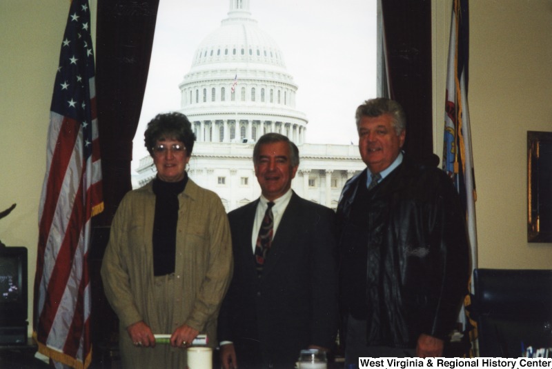 Representative Nick J. Rahall (D-W.Va.) stands between an unidentified man and woman in his office.