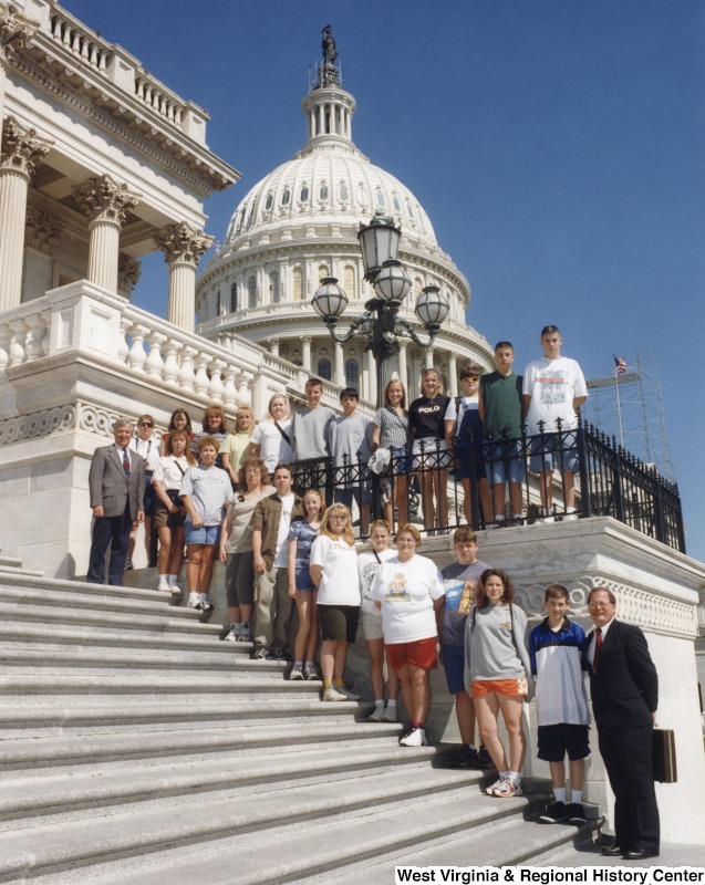 At the top of the stairs, Representative Nick J. Rahall (D-W.Va.) stands with an unidentified group of school students in front of the Capitol building.