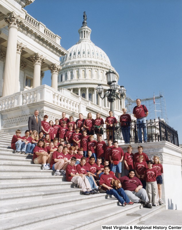 On the far left, Representative Nick J. Rahall (D-W.Va.) stands with an unidentified group of children in red shirts in front of the Capitol building.