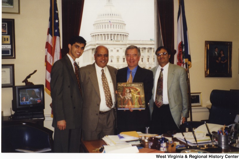 Congressman Nick Rahall (D-WV) holding a book with three unidentified men in his D.C. office.