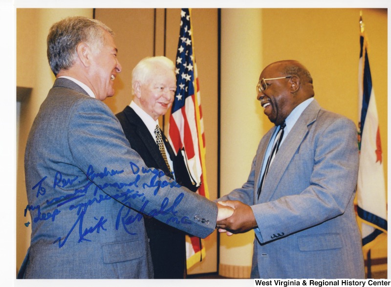 Congressman Nick Rahall (D-WV) and Senator Robert C. Byrd (D-WV) shaking hands with Reverend Dugan. Photograph is Signed: "To Reverend Andrew Durgan, my warmest personal regards and deepest appreciation, Nick Rahall M.C."