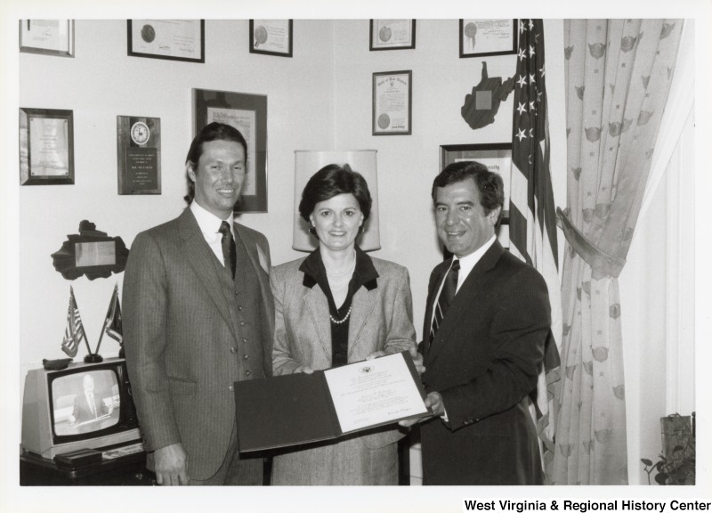 On the right, Representative Nick J. Rahall (D-W.Va.) presents a folder to an unidentified woman and an unidentified man.