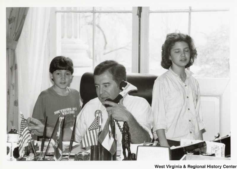 Representative Nick J. Rahall (D-W.Va.) sits at his desk on the telephone between two unidentified children.